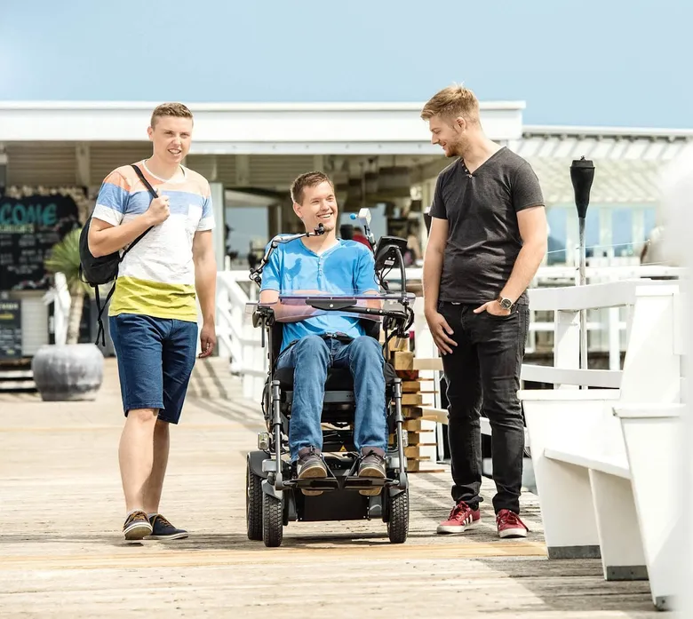 Junger Mann im Elektrorollstuhl unterwegs mit Freunden