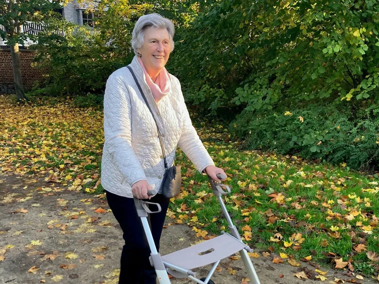 Lächelnde ältere Frau mit Leichtgewichtrollator beim Herbstspaziergang im Park