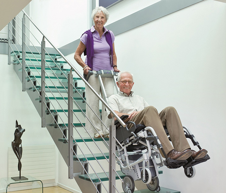 Älterer Mann wird im Rollstuhl mit einem Treppensteiger sicher die Treppe hinaufgefahren